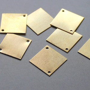 Puede incluir: Un grupo de siete placas cuadradas de metal de color latón con dos agujeros cada una. Las placas están esparcidas sobre una superficie gris.