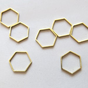 May include: Six gold-colored metal hexagonal rings, or jump rings, on a white surface.