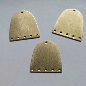 May include: Three gold-toned metal arches with five holes each. The arches are slightly curved and have a textured surface.