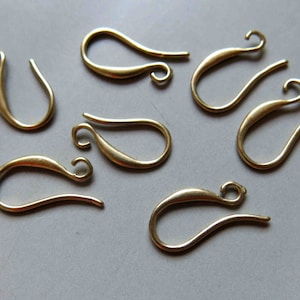 Op de afbeelding: Een set van tien gouden metalen oorhaken. De haken zijn traanvormig met een kleine lus aan de bovenkant.