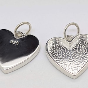May include: Silver heart charm pendant with a smooth front and a textured back. The back of the charm is marked with "925".