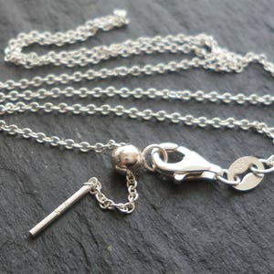 May include: A silver necklace with a fine chain and a lobster clasp. The necklace includes a small, cylindrical bar with a single gemstone. The chain is approximately 45 cm long.