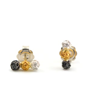 Puede incluir: Un par de pendientes de plata con tres esferas texturizadas en negro, oro y plata.