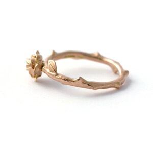 May include: A rose gold ring with a delicate rose design and a twig-like band.