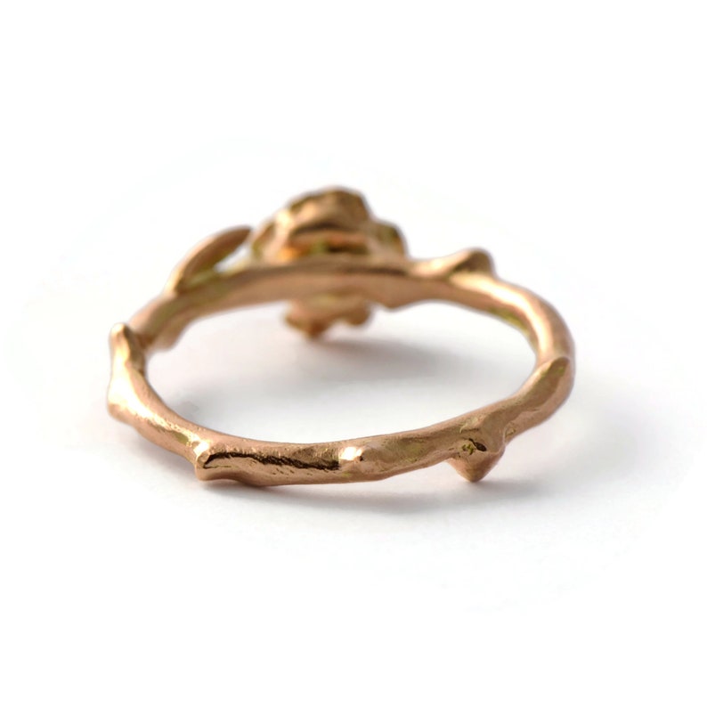 May include: A rose gold ring with a rose design. The ring is made to look like a thorny branch.