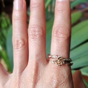 May include: A pair of gold rings with a rose design. The rings are worn on a person's finger.