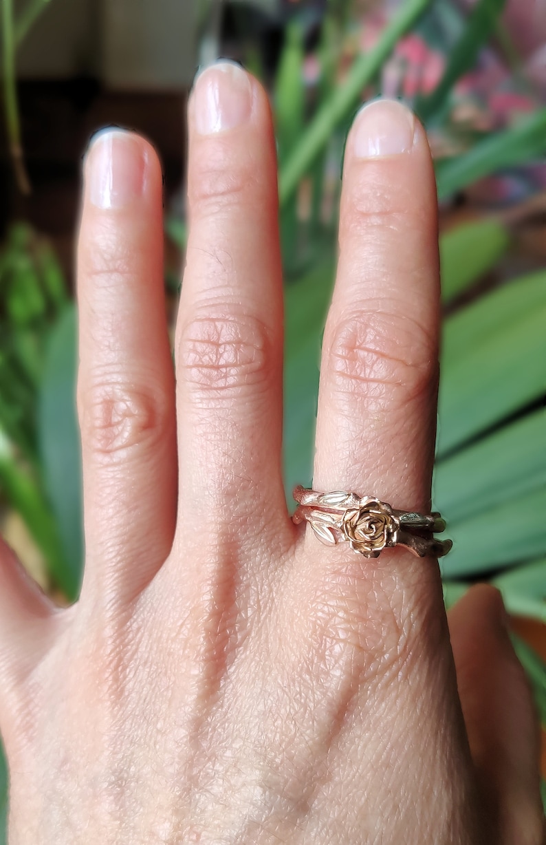 May include: A pair of gold rings with a rose design. The rings are worn on a person's finger.