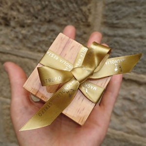 May include: A small wooden box tied with a gold ribbon. The ribbon has the text "Magnolia Strepo" printed on it.