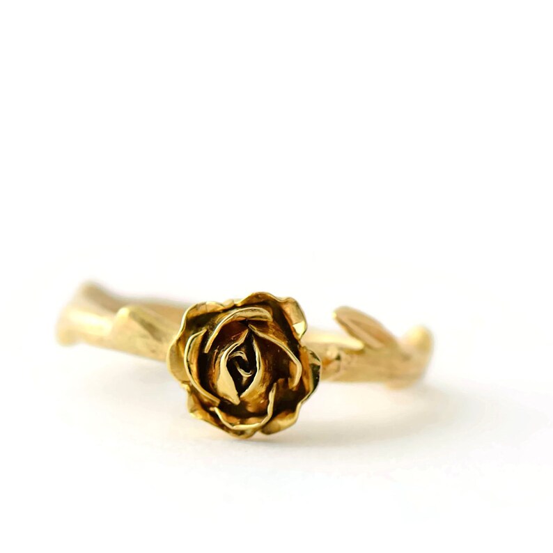 May include: A gold ring with a rose design. The rose is sculpted in detail and sits on a branch-like band.