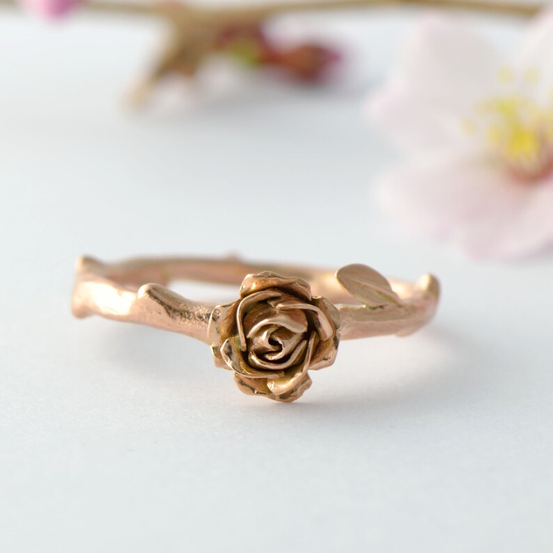 May include: A rose gold ring with a rose design on a twig-like band.