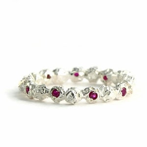 May include: A silver band ring with a textured surface and small red gemstones set in the band.