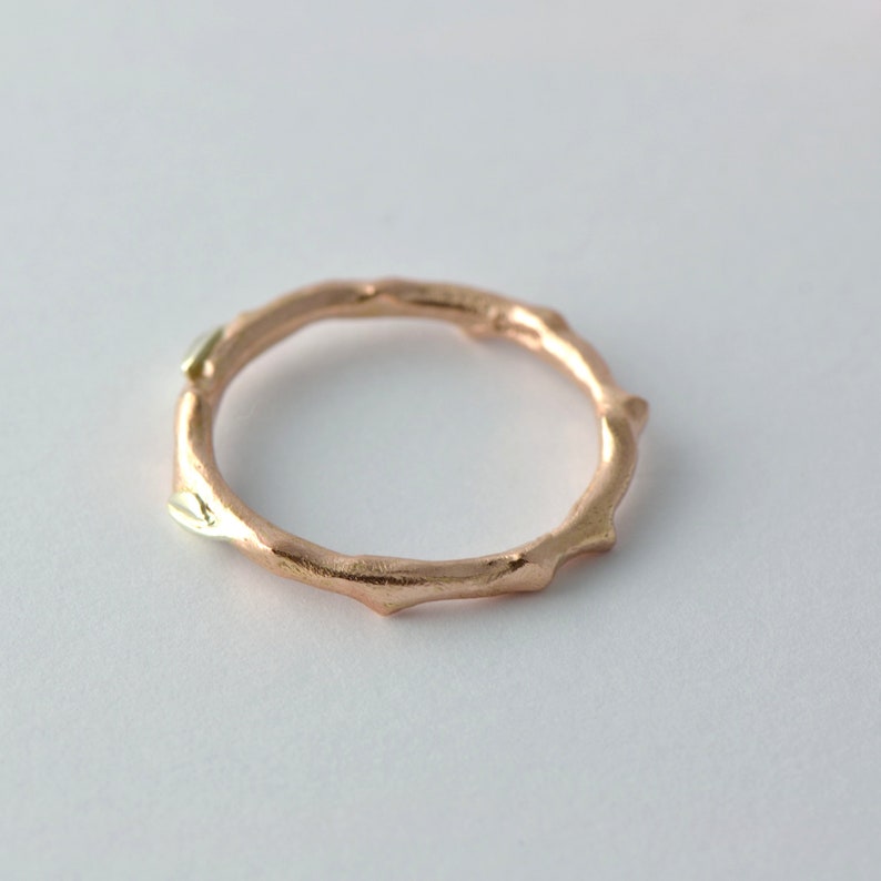 Puede incluir: Un anillo de oro rosa con un dise&ntilde;o texturizado en forma de rama. El anillo tiene dos peque&ntilde;os acentos de oro blanco.