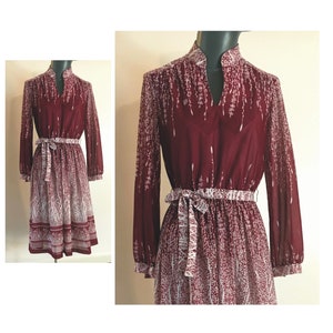 May include: A maroon midi dress with a white floral print and a tie belt. The dress has long sleeves and a V-neck.