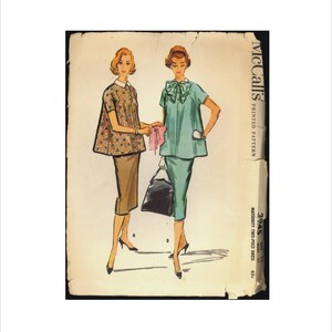 May include: Vintage McCall's sewing pattern for a maternity two-piece dress. The pattern is printed on light brown paper with a vintage look. The pattern shows two women wearing the dress in a light brown and a light blue colour.