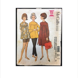 May include: A vintage sewing pattern for maternity clothing. The pattern is for a dress or top and pants or shorts. The pattern is size 12, bust 32, and is printed on a white background with red and black text. The pattern shows three women wearing the different styles.