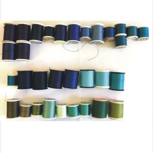 May include: A collection of spools of thread in various shades of blue, green, and black. The spools are arranged in two rows on a white surface.