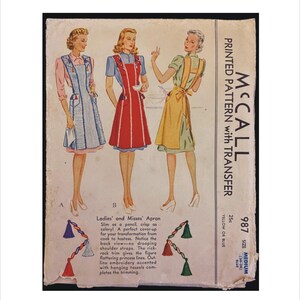 May include: A vintage McCall's sewing pattern for a ladies' and misses' apron. The pattern is printed on a white background with a yellow and blue color scheme. The pattern includes a transfer and is for size medium (34-38). The pattern shows three women wearing different versions of the apron, one in red, one in blue, and one in green.