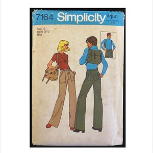 May include: Vintage Simplicity sewing pattern 7164. The pattern features illustrations of two people wearing flared pants and carrying bags. The pattern includes sizing information: Size 12, Waist 26 1/2 inches. The pattern is in a blue and white color scheme.