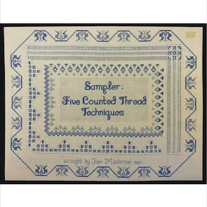 以下が含まれることがあります： クリーム色の背景に青い刺繍が施された、額装されたテキスタイルサンプラー。 サンプラーには「Sampler: Five Counted Thread Techniques」というテキストがあり、装飾的なボーダーで囲まれています。 「wrought by Joan Masterson 1982」というテキストも含まれています。