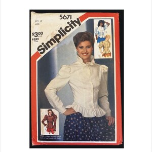 May include: A Simplicity 5671 sewing pattern envelope for a size 10 miss blouse. The cover features a white long-sleeve button-up shirt with a ruffled collar, puffed shoulders, and a ruffled hem, alongside smaller illustrations of variations.