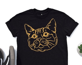 May include: Black t-shirt with a gold outline of a cat's face.