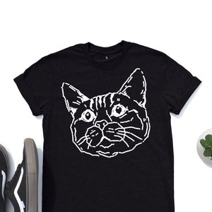 Puede incluir: Camiseta negra con un contorno blanco de la cara de un gato.