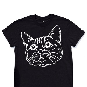 Puede incluir: Camiseta negra con un contorno blanco de la cara de un gato.