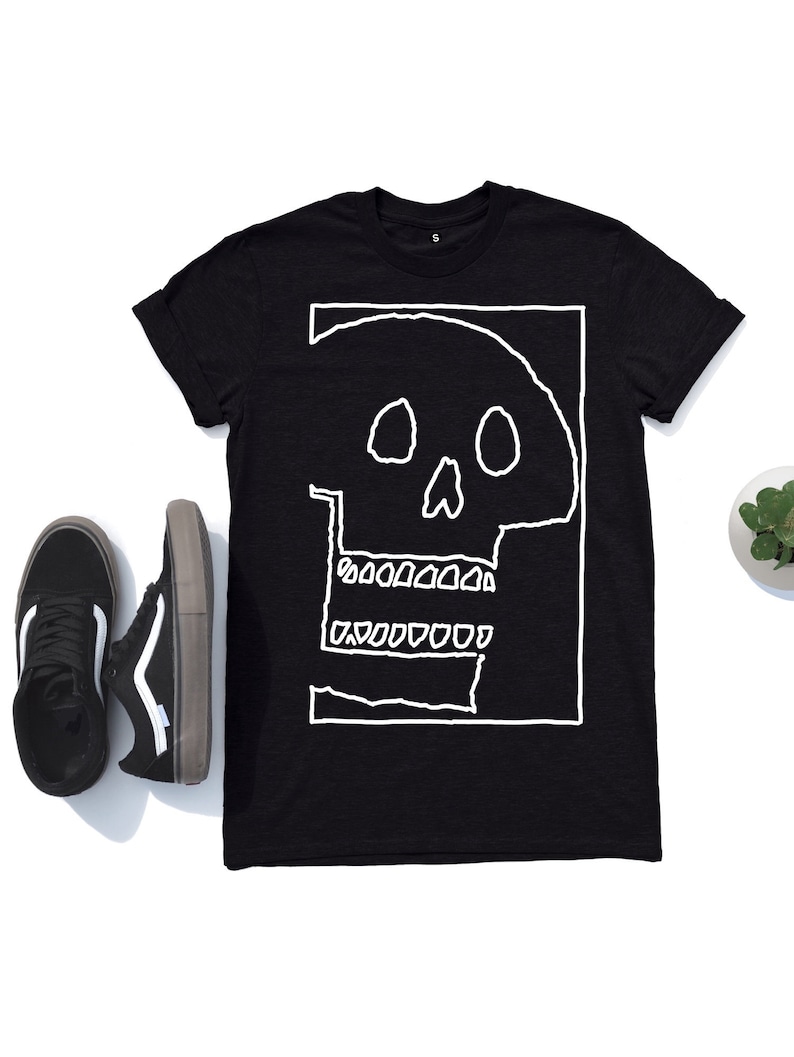 Op de afbeelding: Zwart T-shirt met een witte omtrek van een schedel op de voorkant. De schedel heeft een eenvoudig ontwerp met twee oogkassen, een neus en een mond met tanden.