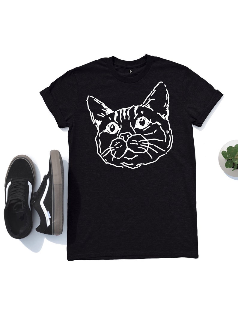 Puede incluir: Camiseta negra con un contorno blanco de la cara de un gato.
