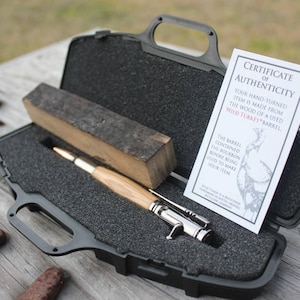 May include: A wooden pen made from a Wild Turkey barrel, with a silver bullet tip and a certificate of authenticity. The pen is in a black carrying case with a foam interior.