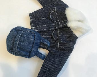 May include: A miniature denim jacket and backpack set. The jacket is dark blue with white stitching and a white fluffy lining. The backpack is a matching dark blue denim with white stitching and small straps. The set is designed for a doll.