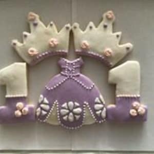 May include: Set of purple and white royal-themed sugar cookies decorated with frosting and pearl sprinkles. The set includes two crowns, a dress, and two number one cookies.