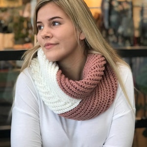 May include: A woman wearing a white long-sleeved shirt with a pink and white knitted infinity scarf.