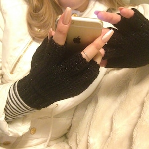 May include: A person wearing black fingerless gloves with a white stripe on the wrist, holding a gold iPhone with a white screen. The person is wearing a white jacket with a zipper and a fur collar.