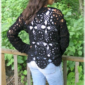 May include: A black crochet cardigan with a lacy pattern. The cardigan is worn over a white shirt and blue jeans.