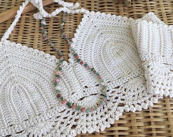 May include: White crochet halter top with a beaded necklace. The top is made with a delicate crochet stitch and has a scalloped edge.