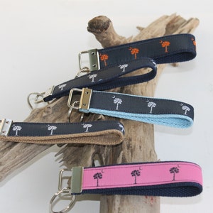 May include: Five keychains with different colored straps and a silver key ring. Each strap features a white palm tree design with a crescent moon.