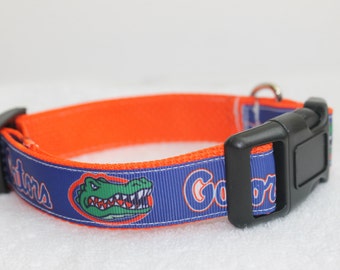 May include: A blue and orange dog collar with a black buckle. The collar has a printed image of an alligator with the word "Gators" on it.