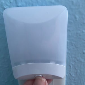 May include: A white plug-in night light with a rounded rectangular shape and a small button on the bottom.