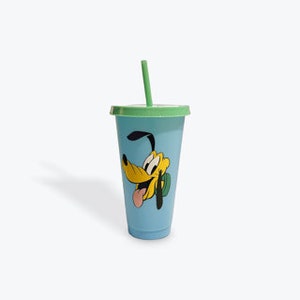 Peut inclure: Un gobelet réutilisable bleu avec un couvercle et une paille verts. Le gobelet présente une image de dessin animé de Pluto, un chien jaune avec un collier vert, tirant la langue.