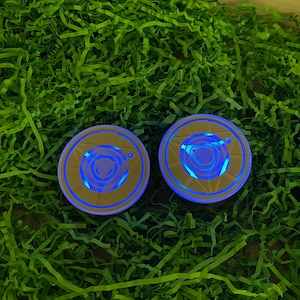 Puede incluir: Dos posavasos redondos, azules y dorados, con un diseño geométrico. Los posavasos están sobre una cama de papel verde triturado.
