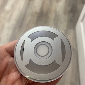 May include: A silver-colored round button with a white circle in the center and a stylized green lantern symbol around the circle.