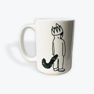 May include: White ceramic mug with a black line drawing of a person wearing a crown and a tail. The person is facing away from the viewer.