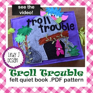 May include: A felt quiet book titled "Troll Trouble" with a purple cover. The cover features a gray felt cave with a troll face, green felt trees, and the text "Troll Trouble." A circular logo reads "Lindy J Design." The text "felt quiet book .PDF pattern" is also visible.