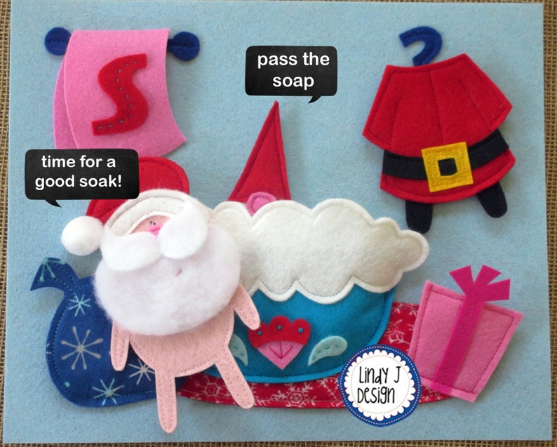 Op de afbeelding: Een vilt speelset met een kerstmanfiguur, een badkuip, een stuk zeep, een cadeau en een bord met de tekst "time for a good soak!"  De set is ontworpen voor kinderen om mee te spelen en te leren over badtijd.