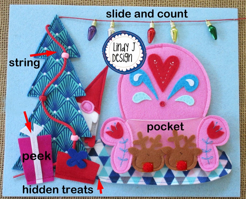 Op de afbeelding: Een vilten speelmat met een roze zak, een blauw-groene kerstboom, een rood-wit cadeau en een rood touwtje met lampjes. De tekst "slide and count" en "Lindy J Design" staan op de mat.
