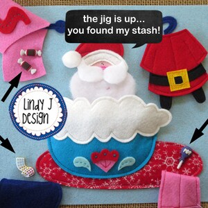 Op de afbeelding: Een vilt knutselset met een kerstmanfiguur in een blauwe en witte slee. De set bevat viltstukken voor de kerstman, de slee en andere kerstthema-artikelen. De tekst "the jig is up... you found my stash!" staat op een zwarte spraakballon.