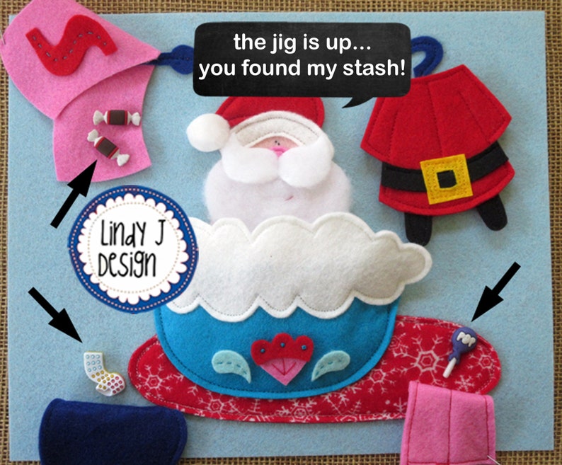 Op de afbeelding: Een vilt knutselset met een kerstmanfiguur in een blauwe en witte slee. De set bevat viltstukken voor de kerstman, de slee en andere kerstthema-artikelen. De tekst "the jig is up... you found my stash!" staat op een zwarte spraakballon.