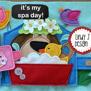 Puede incluir: Una p&aacute;gina de libro de fieltro con un perro tomando un ba&ntilde;o. El perro lleva una corona de flores y est&aacute; en una ba&ntilde;era roja con espuma blanca. El texto "it's my spa day!" est&aacute; escrito en una pizarra negra. El texto "Lindy J Design" est&aacute; escrito en un c&iacute;rculo rojo.