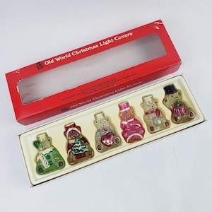 May include: A set of six vintage Christmas light covers shaped like teddy bears, each with unique festive attire. The covers are in a white tray inside a red box labeled "Old World Christmas Light Covers."